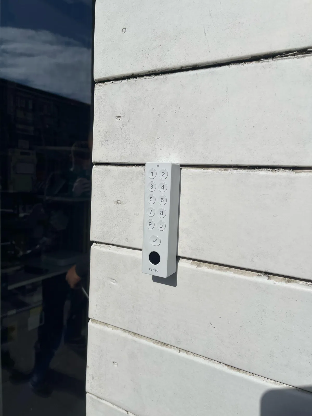 Tedee-keypad met cijfers en vingerafdrukscanner naast de deur op een lichte gevel