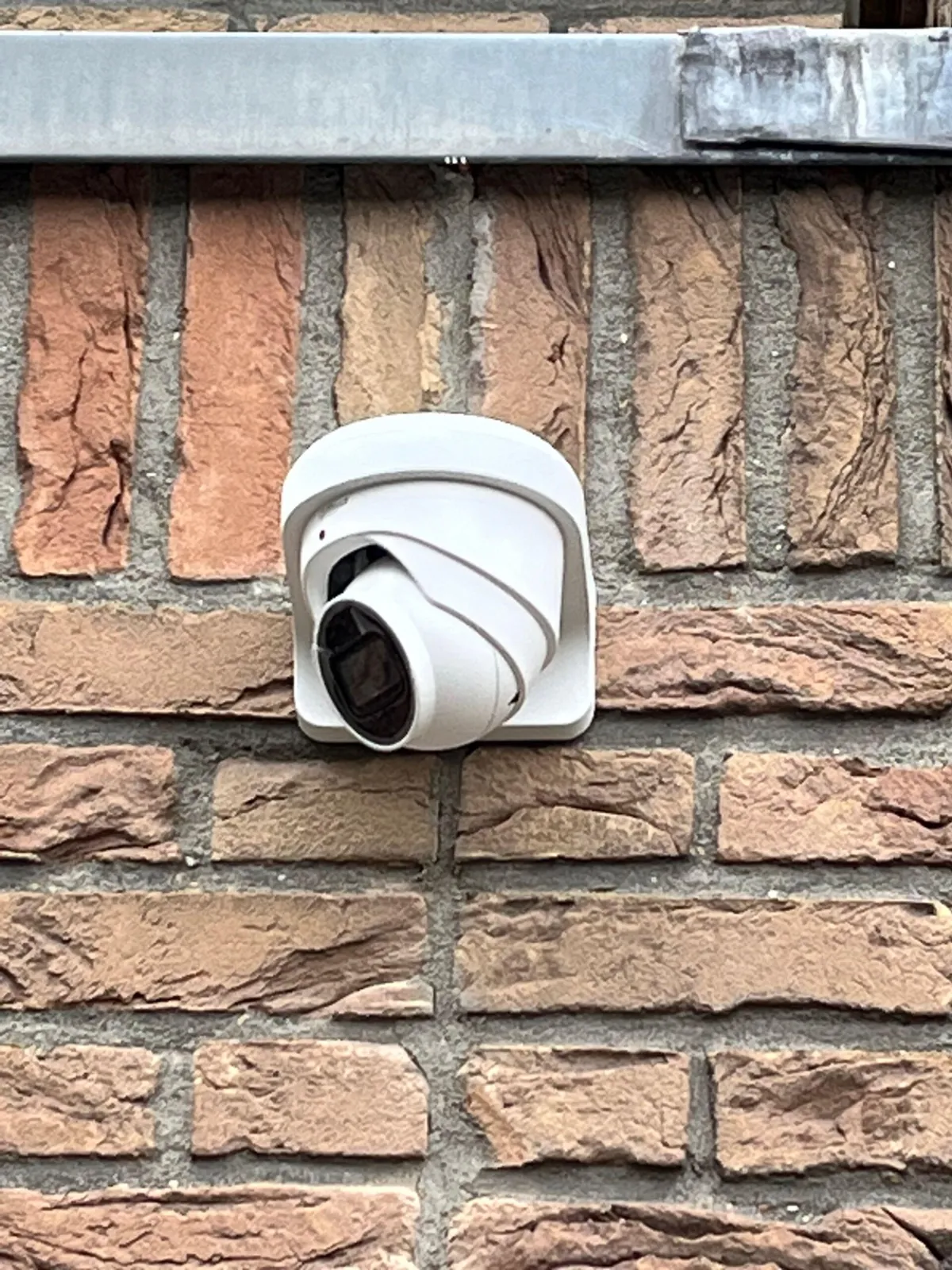 Witte turretcamera onder een zinken daklijst op een bakstenen woning in Diemen
