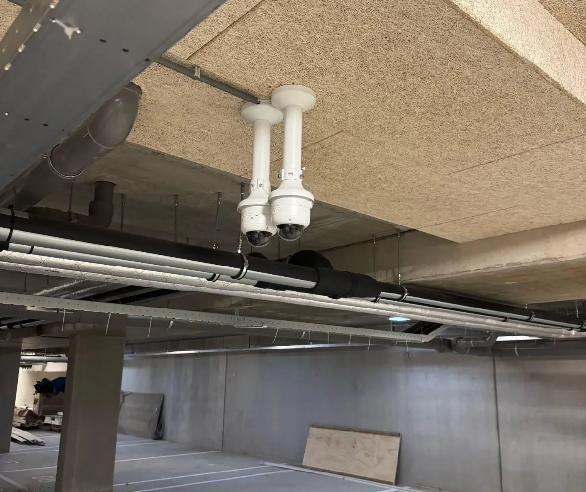 Twee witte turretcamera's op verlengde beugels onder het plafond van een VvE-parkeergarage