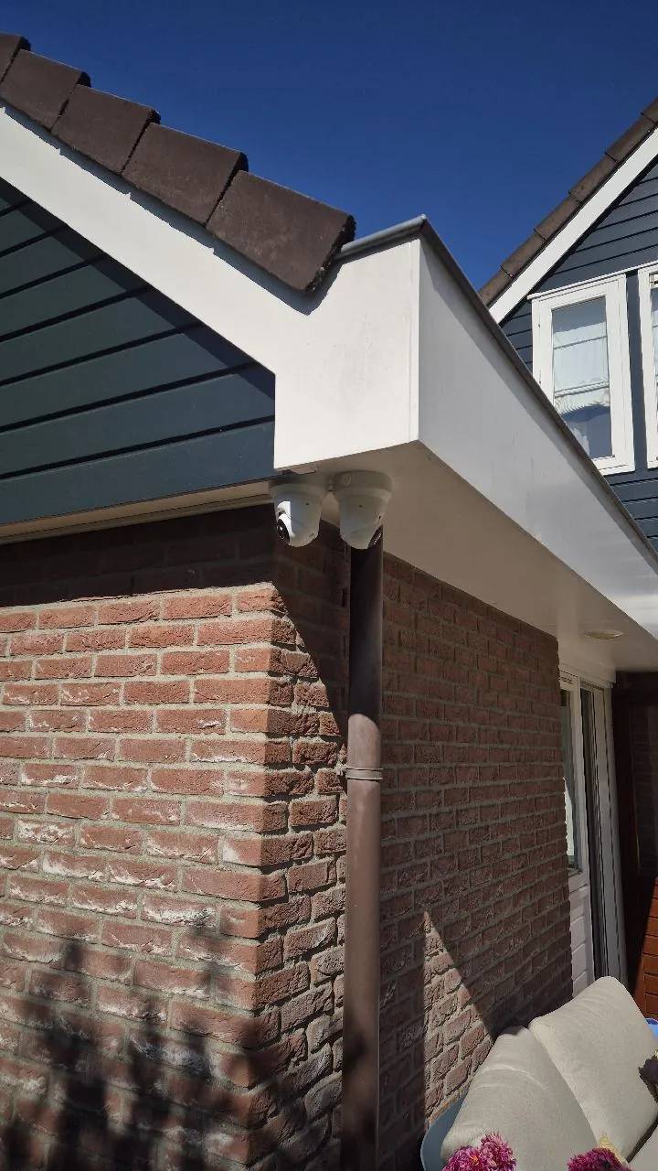 Twee Ajax-domecamera's onder de witte dakrand op de hoek van een bakstenen woning
