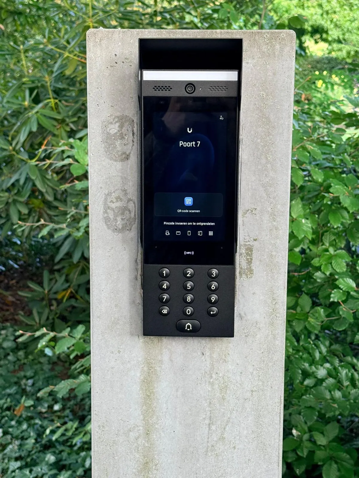 UniFi Access-deurstation in een betonnen zuil bij de poort, met het poortnummer op het scherm