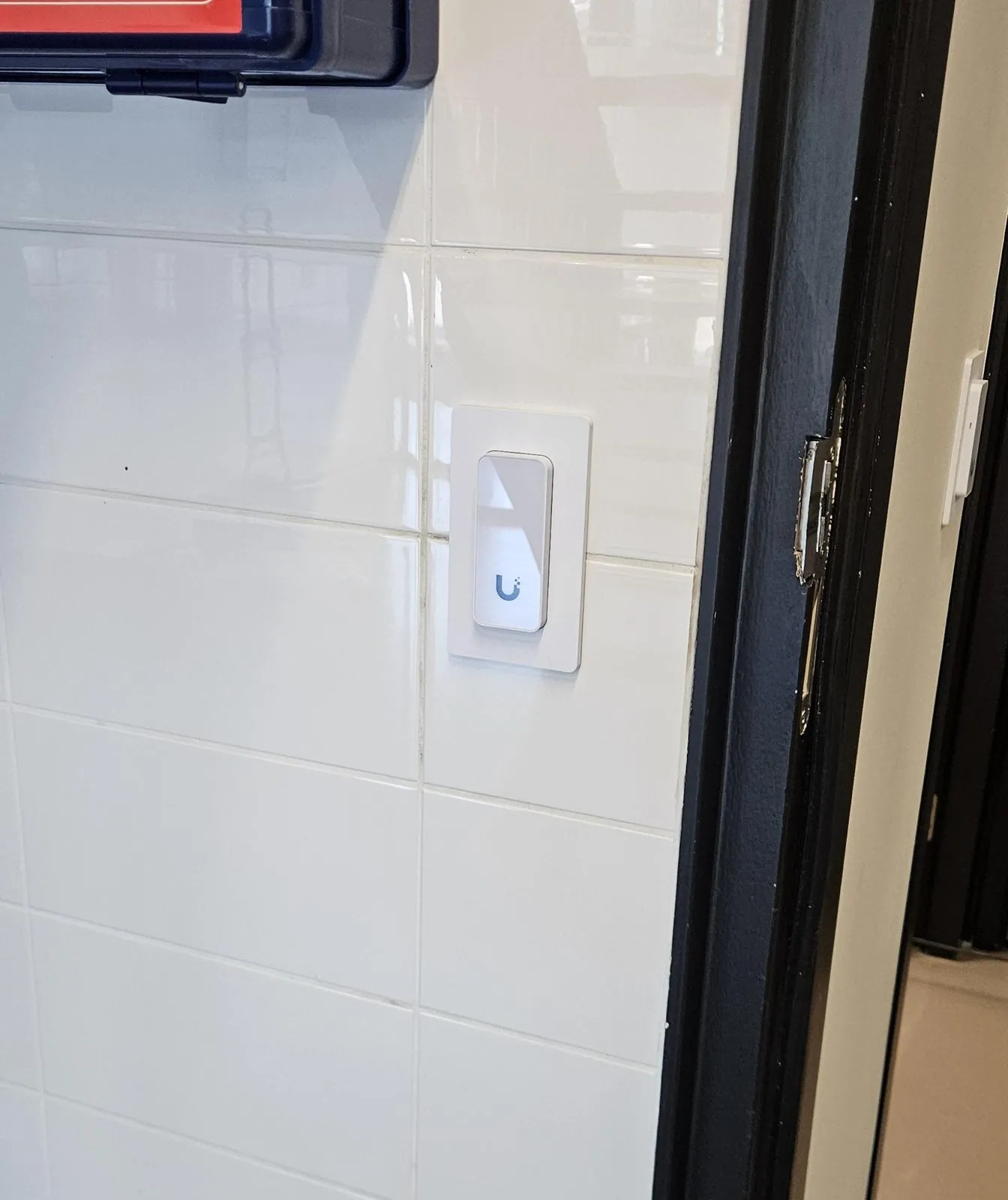 Witte UniFi-lezer strak ingebouwd in een tegelwand naast een zwart kozijn