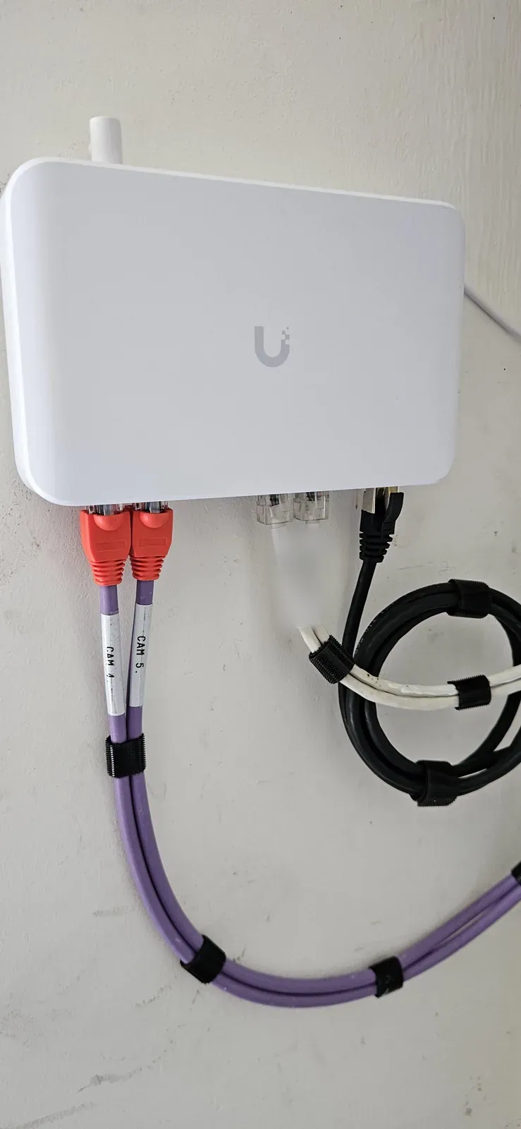 Witte UniFi PoE-switch aan de wand met gelabelde camerakabels, bij een woning in De Ronde Venen
