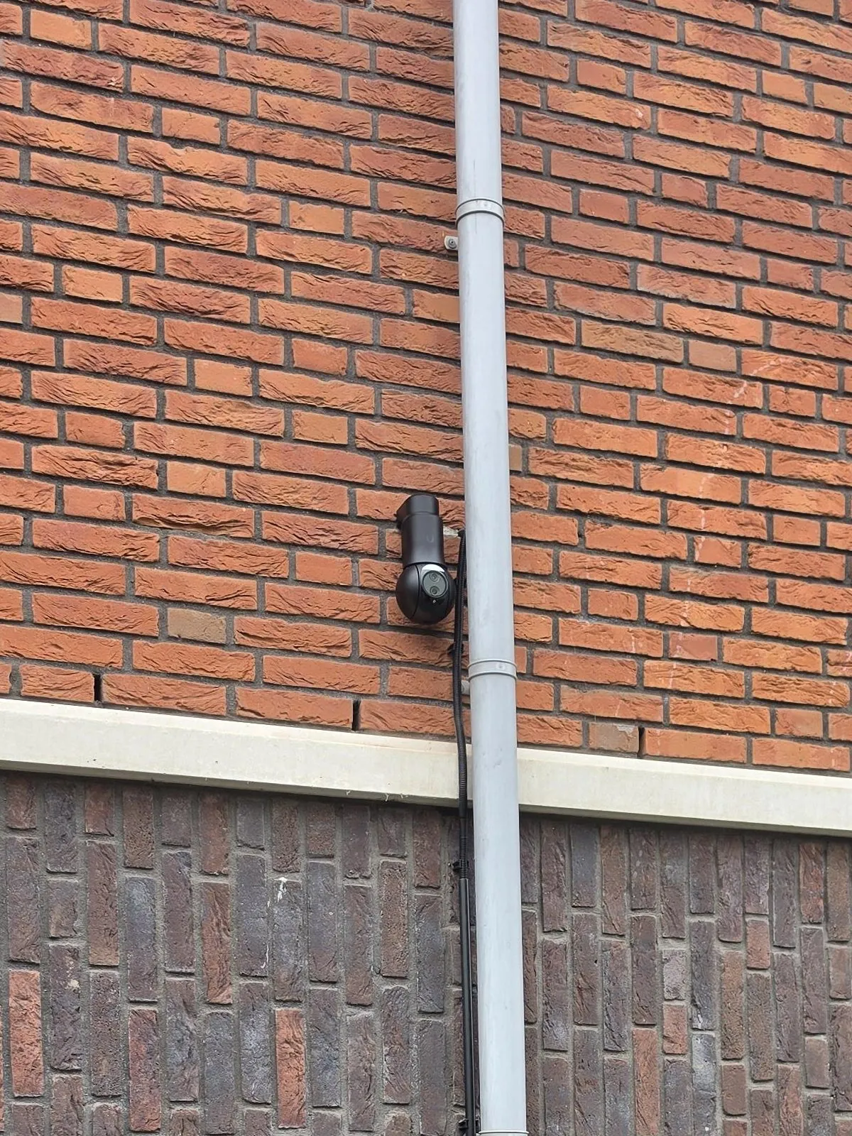 Zwarte bestuurbare UniFi-camera op een muurarm aan een bakstenen gevel in Ridderkerk
