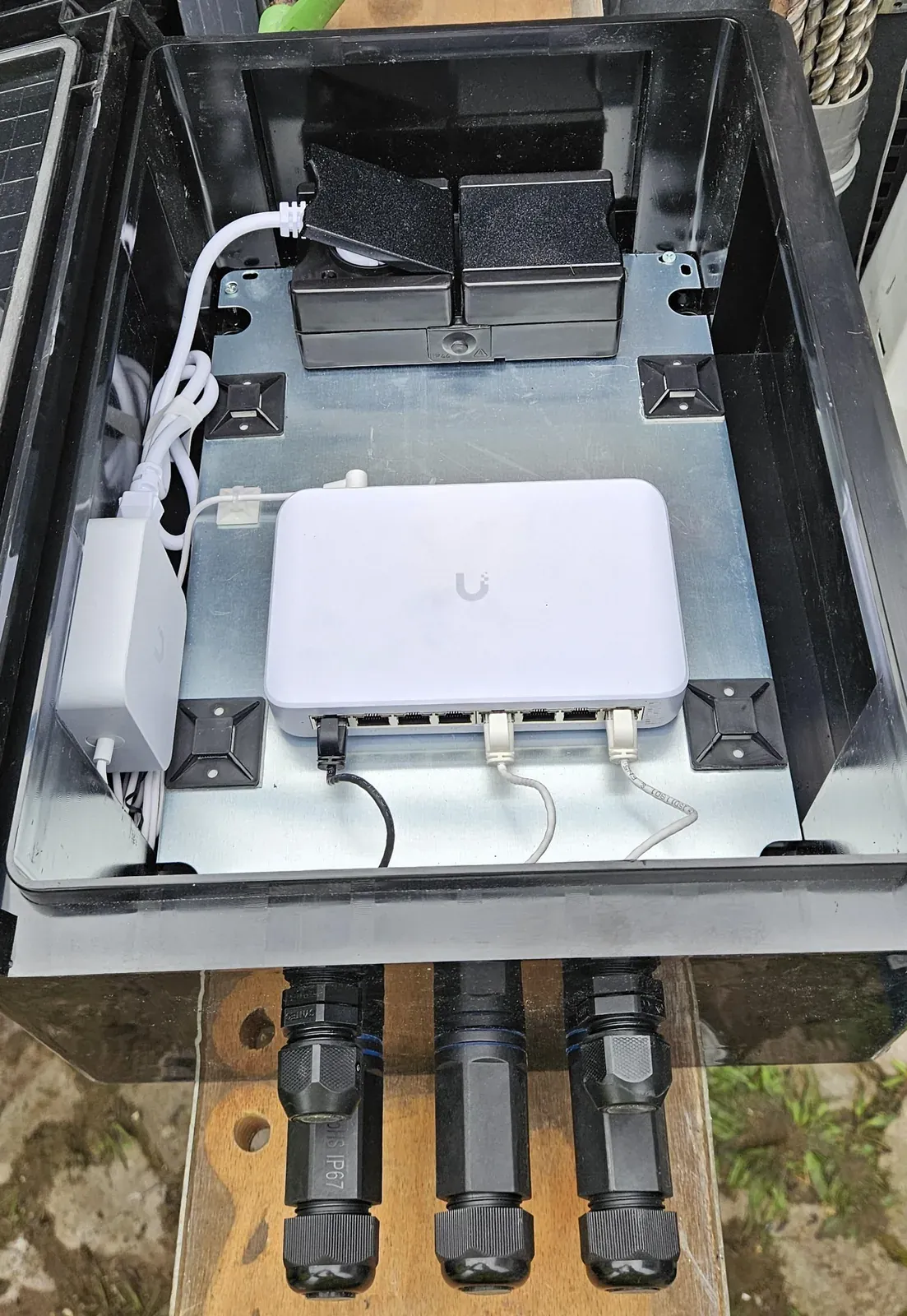 UniFi-switch in een open kunststof kast op een bedrijfsterrein in de Amsterdamse haven, met waterdichte kabeldoorvoeren