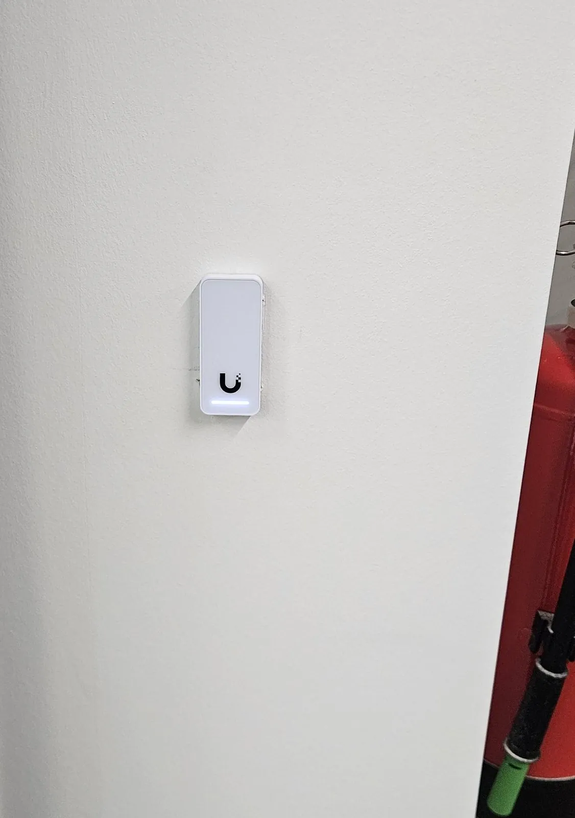 Witte toegangslezer van UniFi met blauw licht naast de deur