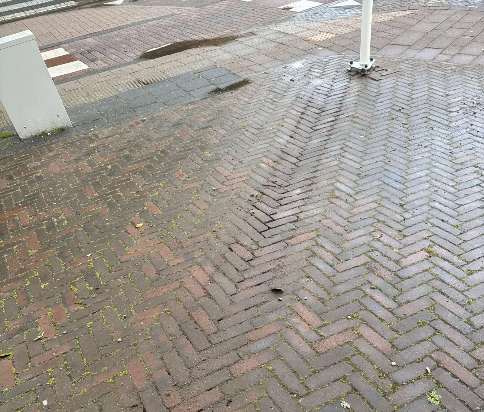 Onderkant van de vlaggenmast tussen rode visgraatklinkers op de stoep in Oosterbeek