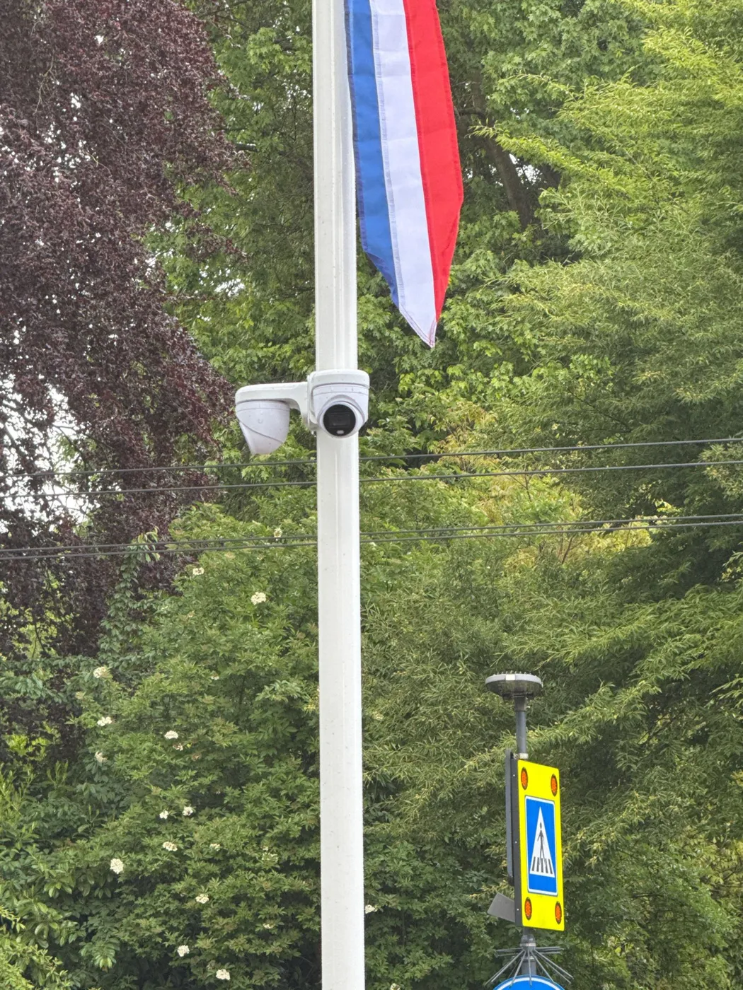 Twee witte UniFi-camera's halverwege een vlaggenmast in Oosterbeek, met de vlag erboven