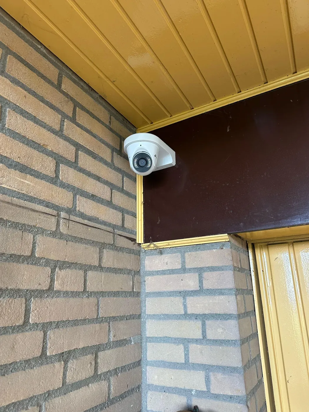 Witte VIGI-camera op een hoekbeugel onder de gele luifel bij de voordeur in Berlicum