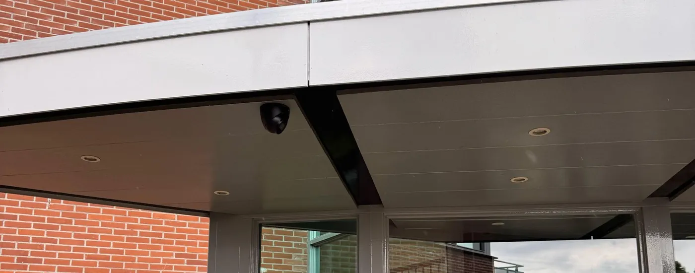 Zwarte Dahua-camera op de hoek van de overkapping boven de glazen entree van een VvE in Ede